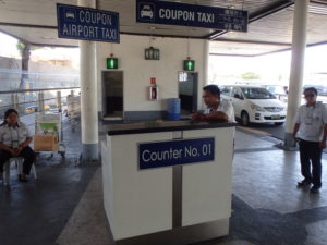 クーポンタクシーの受付デスク。右には白いタクシーが並んでいます。デスクの上の看板にはCoupon　Taxiと書かれています。