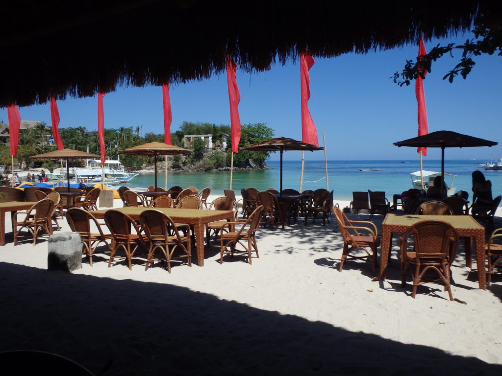白浜の上に屋根付きテーブルと椅子が並べられたマラパスクア島のレストラン